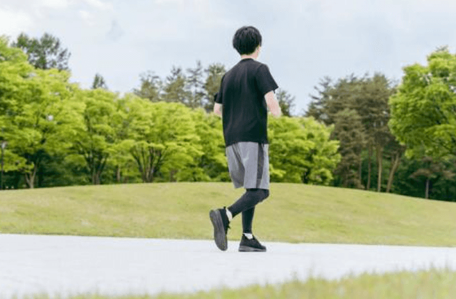 푸른 나무와 잔디가 있는 공원 산책로에서 검은 운동복을 입은 남성이 조깅을 하고 있는 모습.