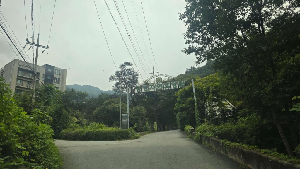 나무와 숲으로 둘러싸인 도로 위에 세워진 “청평자연휴양림” 입구 표지판과 주변 풍경.