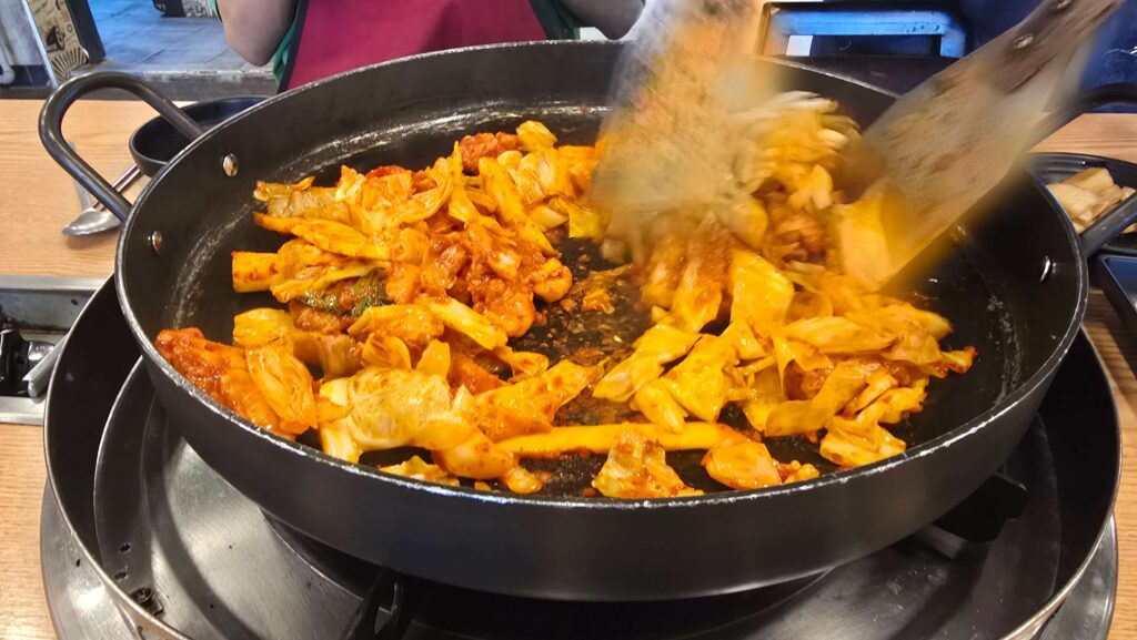 "철판 위에서 양념에 버무린 닭갈비와 채소를 함께 볶는 모습"