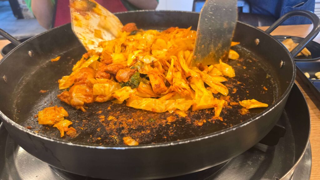 "철판 위에서 양념이 잘 밴 닭갈비와 채소를 골고루 볶는 모습"