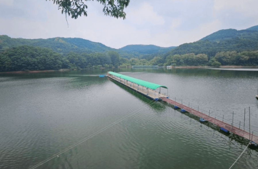 “안성시 죽산면 장계낚시터 전경, 산으로 둘러싸인 저수지 위에 설치된 긴 좌대 시설”
