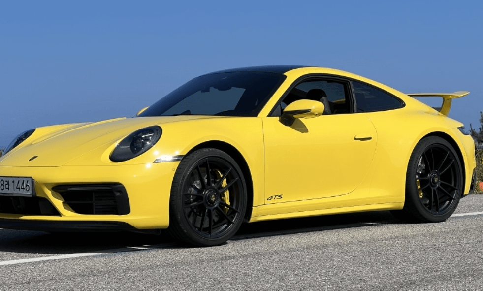 “노란색 포르쉐 911 GTS 스포츠카가 도로 위에 서 있는 모습, 파란 하늘 배경”
